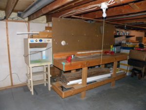 Paint spray booth and existing heavy duty work bench with wood storage behind it. Hot water tank located behind right side of work bench.